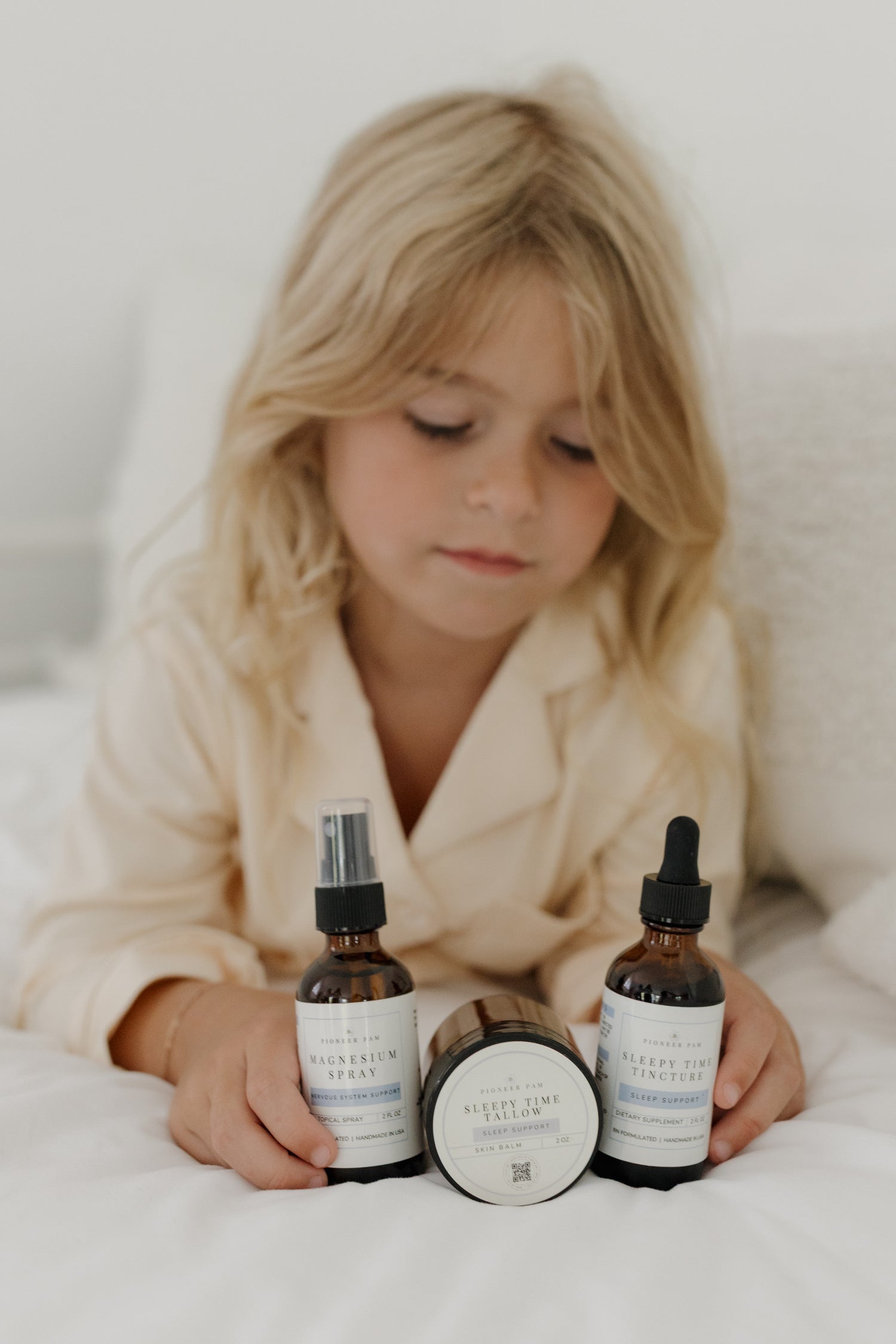 Child in a cozy robe sitting on a bed with Pioneer Pam Sleepy Time Tincture and Tallow