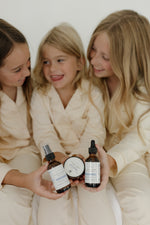 Three children in matching robes sitting together on a bed with Pioneer Pam Sleepy Time products