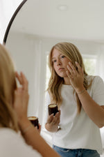 Woman applying Phytotox Tallow moisturizer to her face in front of a mirror