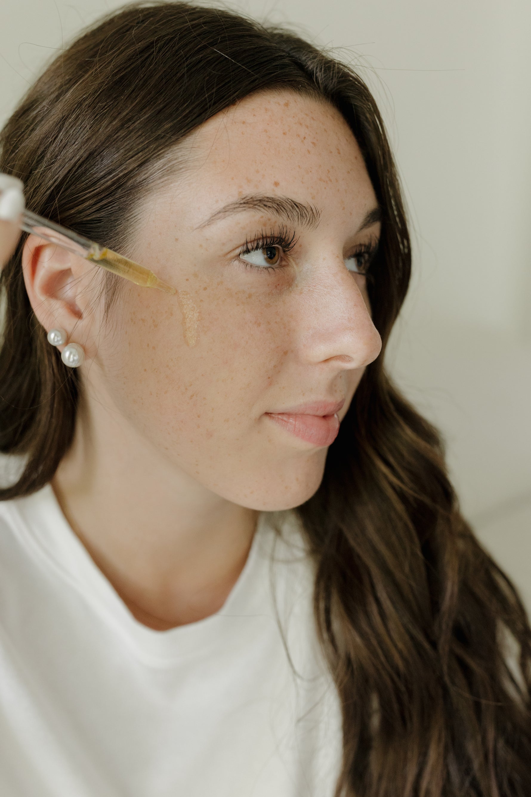Woman applying a facial oil with a dropper near her cheek