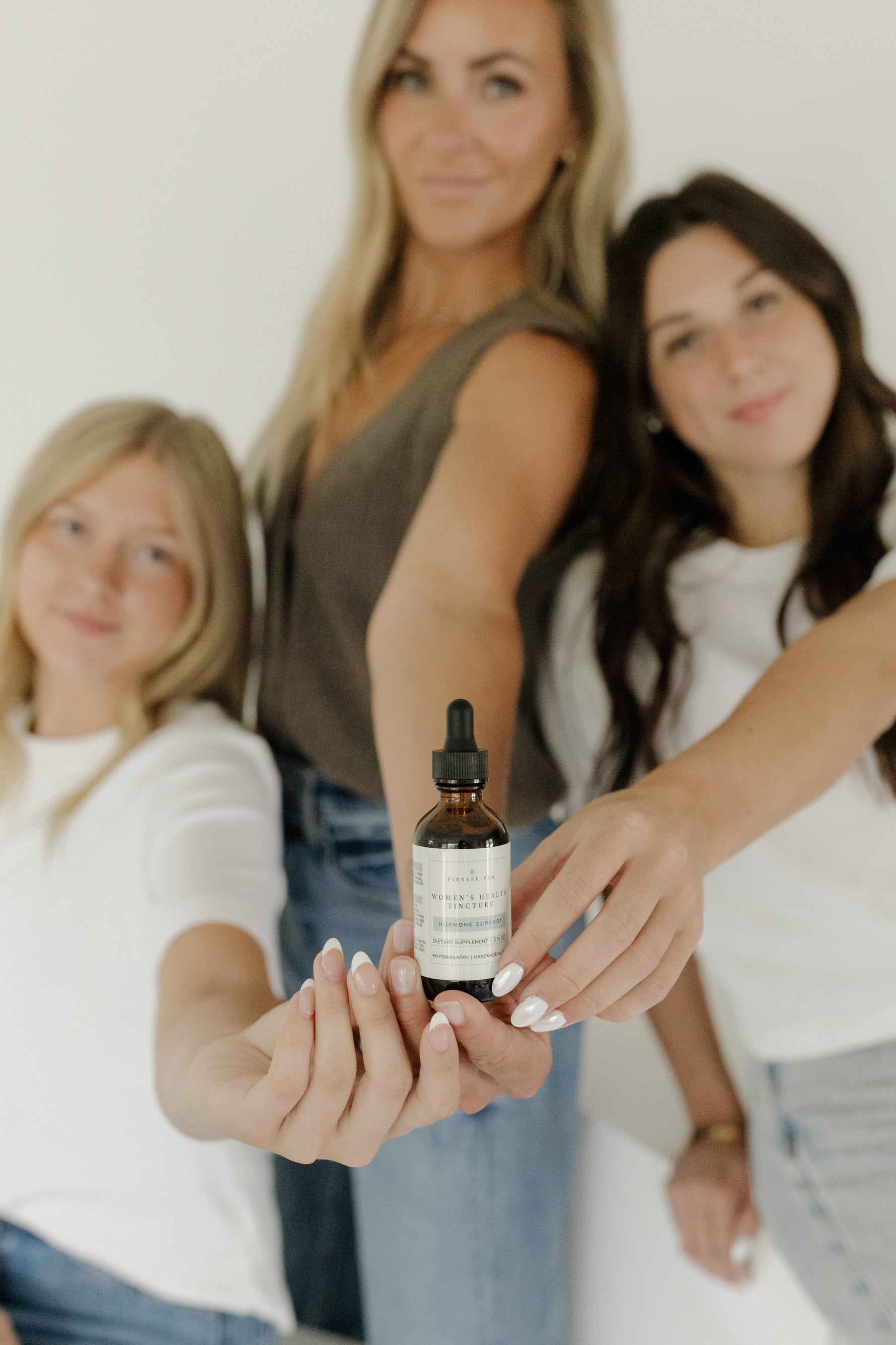 Mother holding a Pioneer Pam Women's Health Tincture dropper bottle, standing with two young daughters
