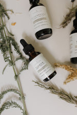 Flat lay of Pioneer Pam herbal tincture bottles, including Yarrow, surrounded by fresh and dried botanical sprigs on a light background.