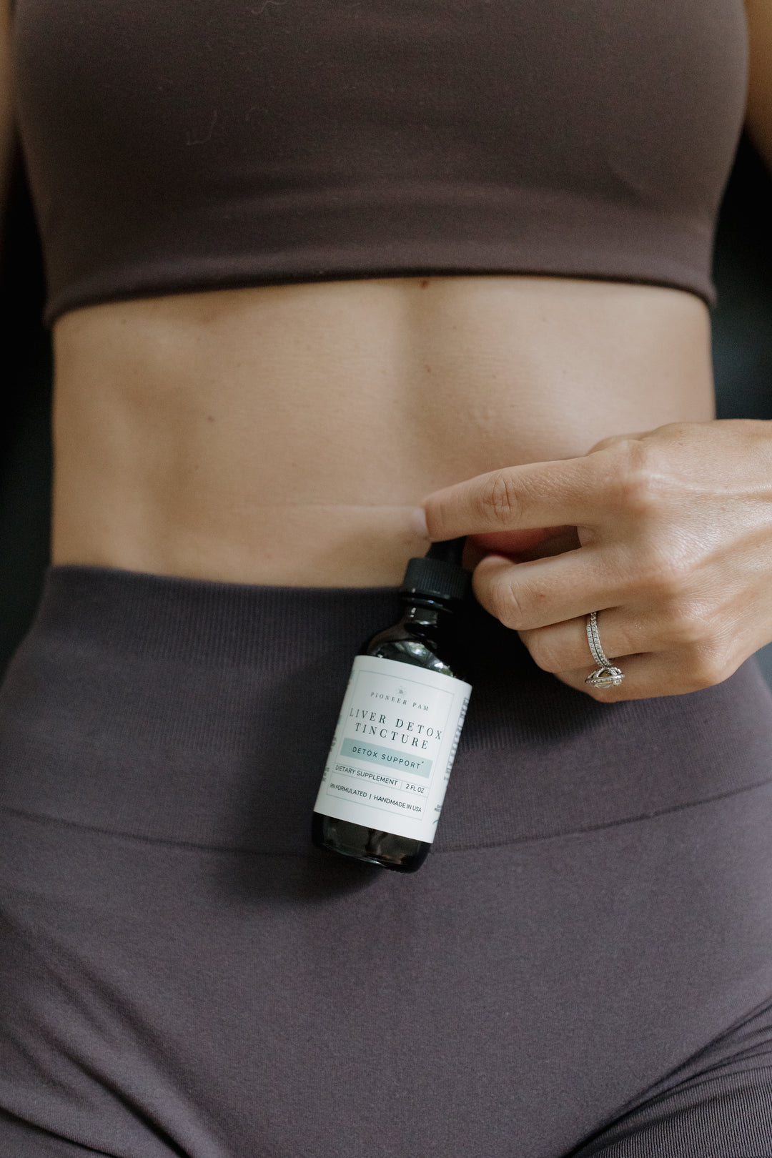 Woman in athletic wear holding a dropper of Pioneer Pam Liver Detox Tincture near her stomach