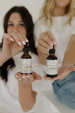 Two women holding amber glass bottles of Pioneer Pam Mullein and Elderberry tinctures.