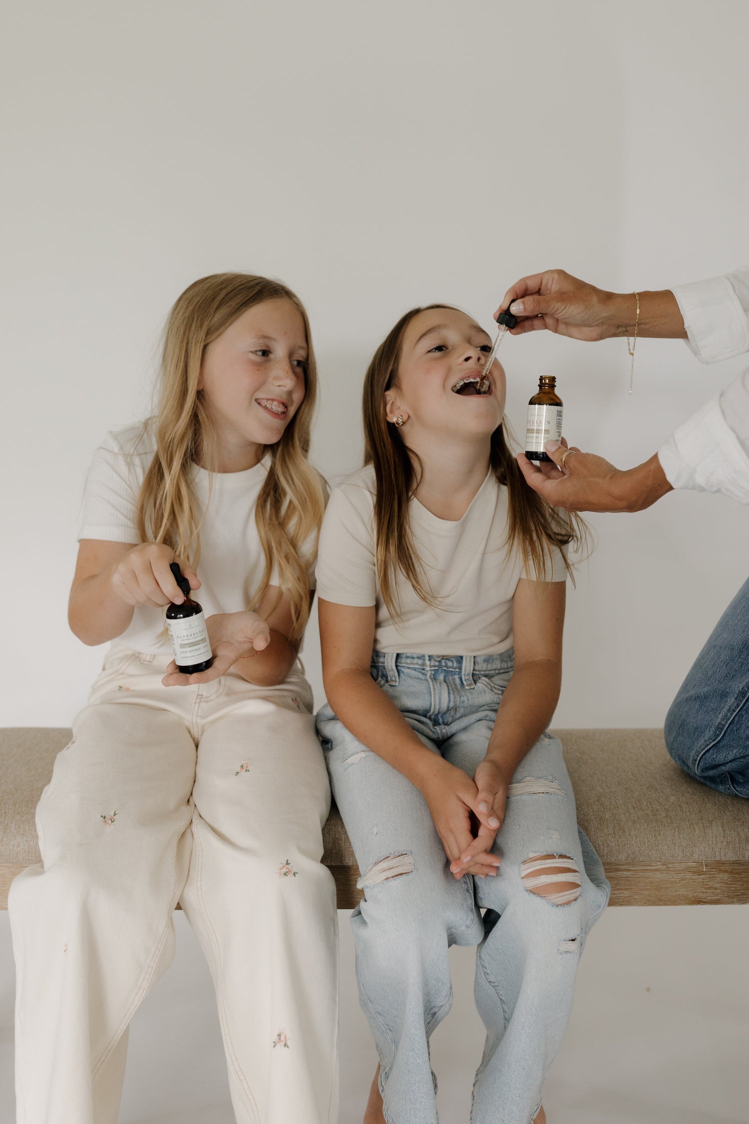 Two children being given herbal tincture drops by an adult, using small amber dropper bottles