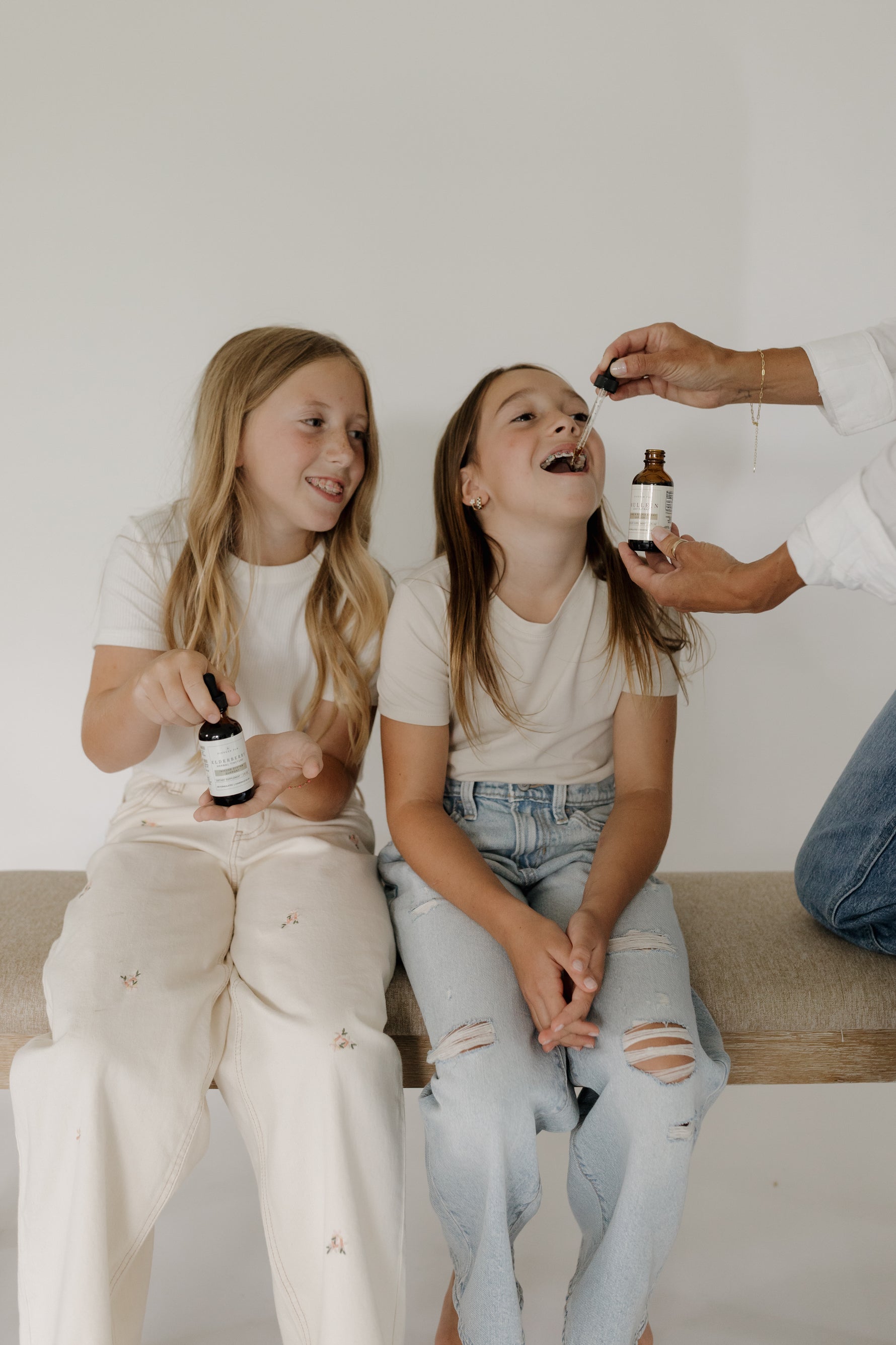 Two children being given herbal tincture drops by an adult, using small amber dropper bottles